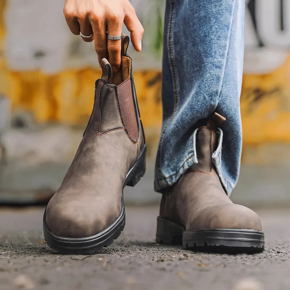 Vintage brown unisex Chelsea boots with a frosted finish, round toe, and low horseshoe heel on a wooden floor.