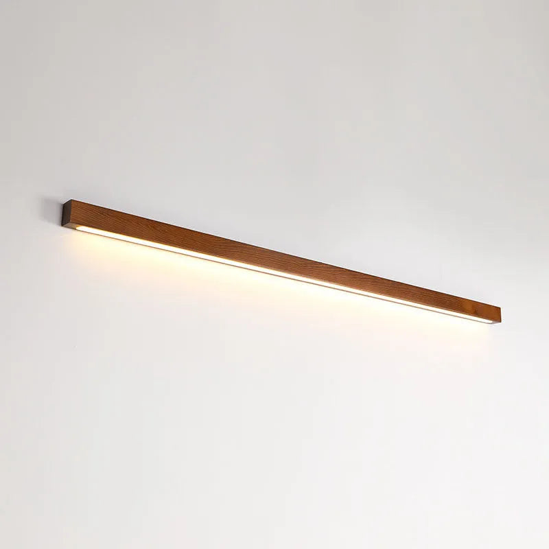 Slim walnut-coloured wooden strip LED wall lamp in three length options on a white wall.