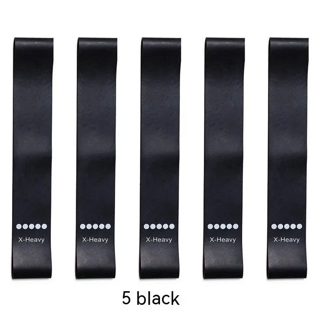 Set of five colour-coded yoga resistance straps in green, blue, yellow, red, and black on a gym mat.