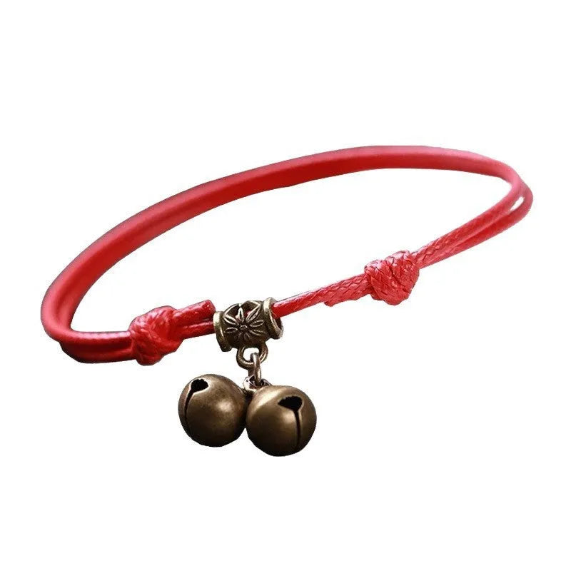 Black nylon rope dog collar with an attached brass bell lying on a wooden surface.
