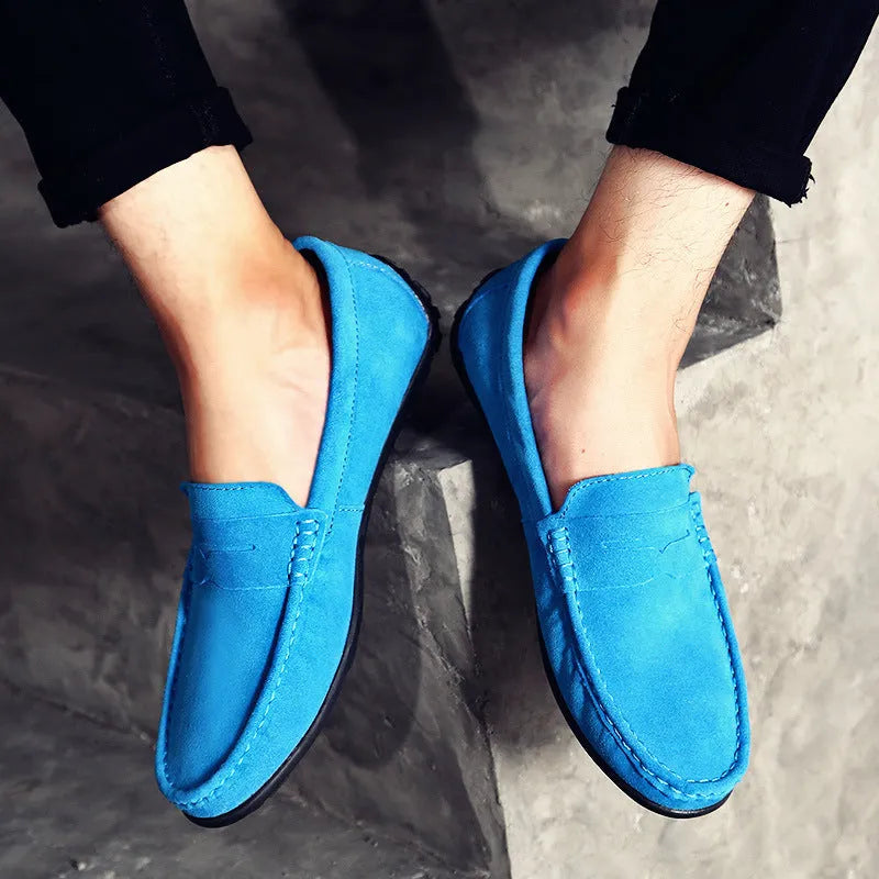 Men's suede slip-on loafers in black on a flat rubber sole, showing round toe and sewing detail.
