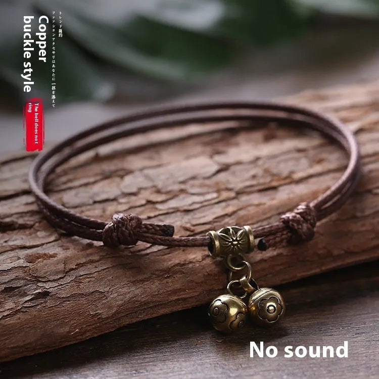 Black nylon rope dog collar with an attached brass bell lying on a wooden surface.