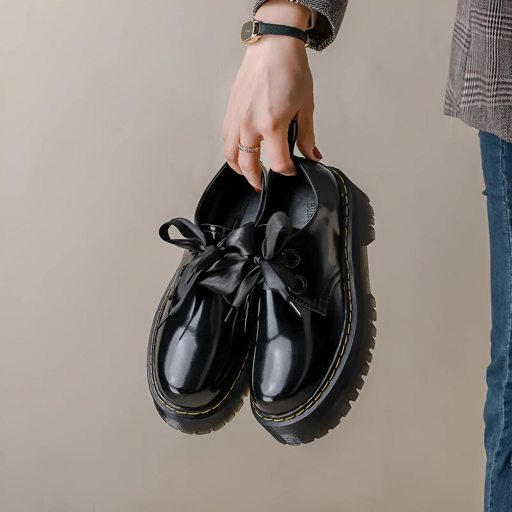 Women's black leather shoes with thick soles, cross straps, and ribbon lacing shown from side view