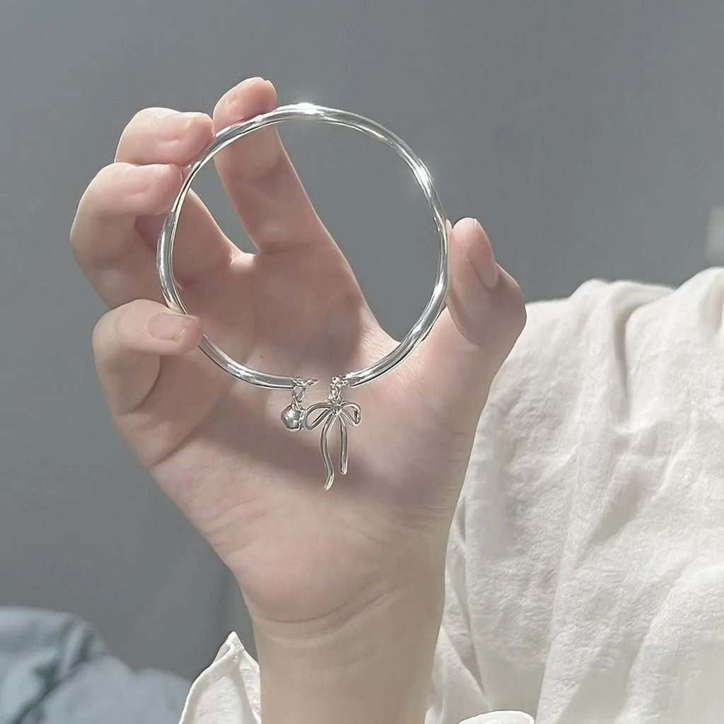 Silver adjustable bracelet with a bow charm and an opening bell charm on a model's wrist.