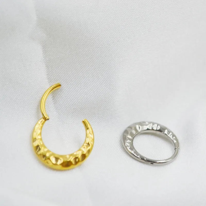 Close-up of a concave-convex carved titanium nose ring in gold finish on a grey background.