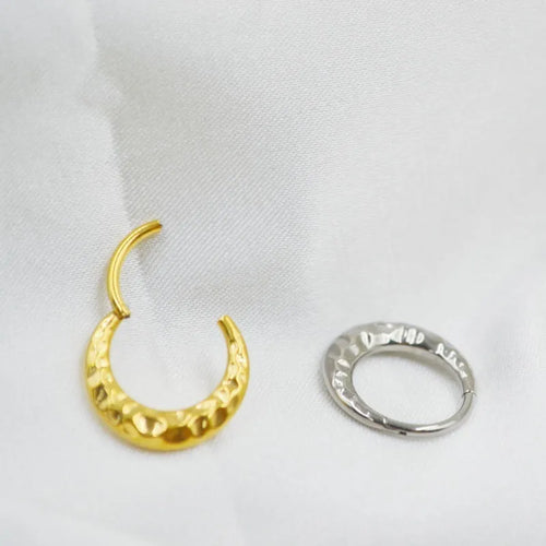 Close-up of a concave-convex carved titanium nose ring in gold finish on a grey background.