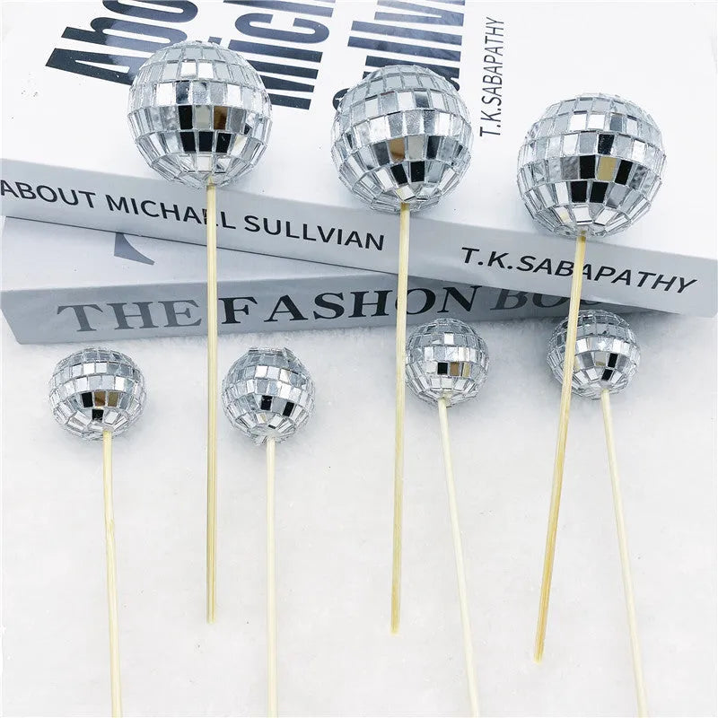 Glass disco ball cake decoration with wooden stick on a cake, showing reflective surface.