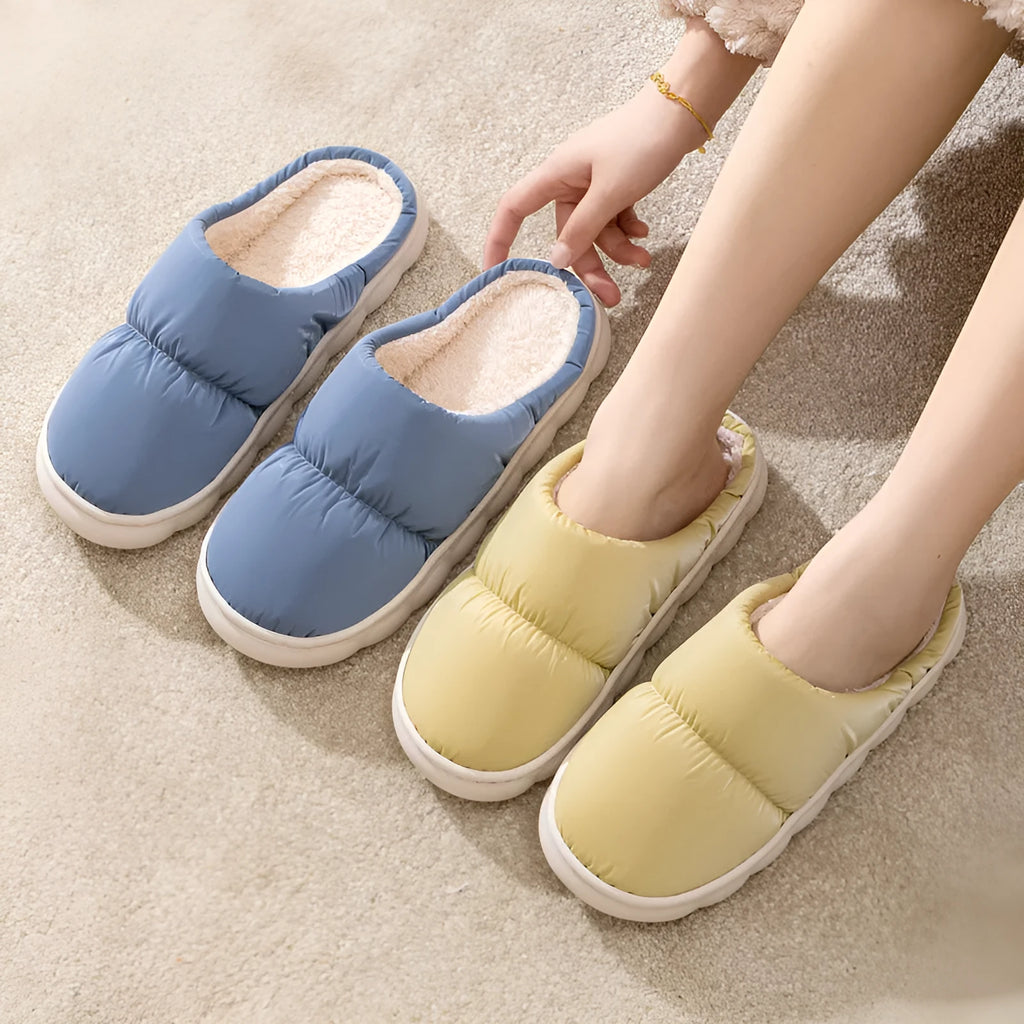 Blue down cotton indoor slippers with thick rubber sole and plush lining on a wooden floor.
