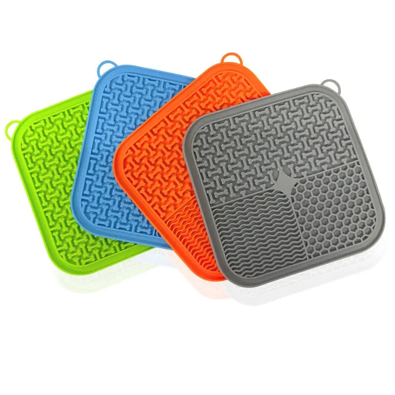 Orange, grey, blue, and green silicone dog licking mat with suction cups on a smooth surface.