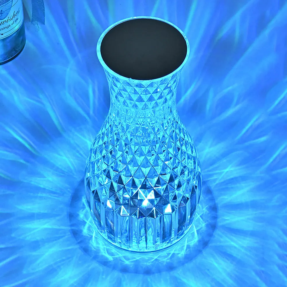 Clear plastic vase-shaped crystal bedside lamp with LED lights on a wooden table.