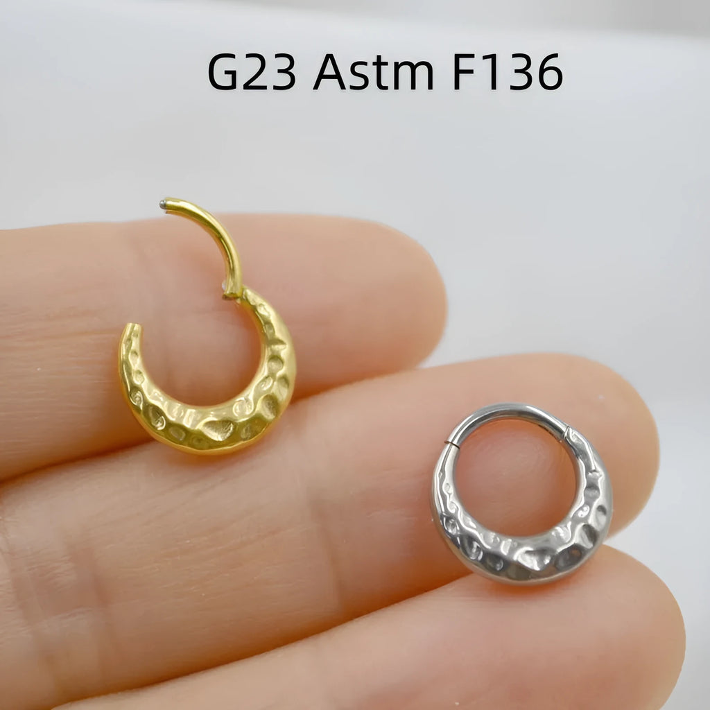Close-up of a concave-convex carved titanium nose ring in gold finish on a grey background.