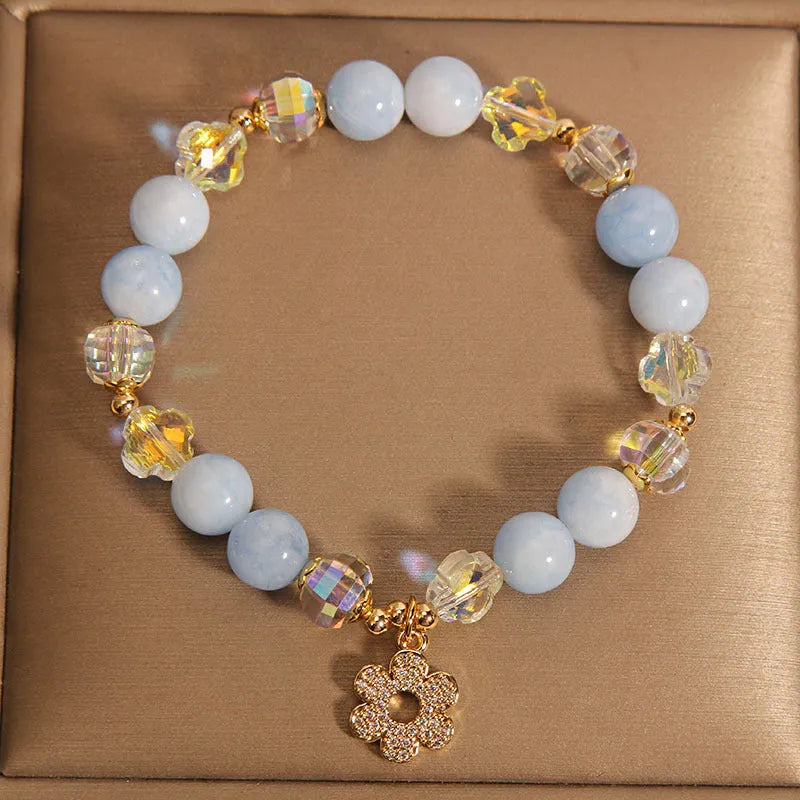 Women's aquamarine crystal bracelet with a four-leaf clover charm and a pearl accent on a model's wrist.