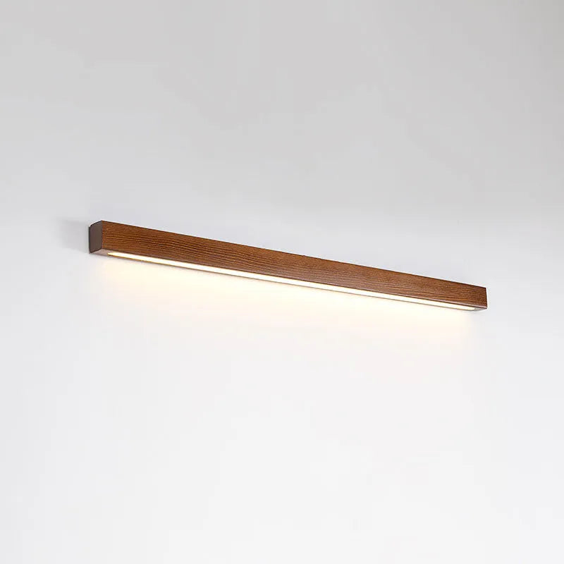 Slim walnut-coloured wooden strip LED wall lamp in three length options on a white wall.