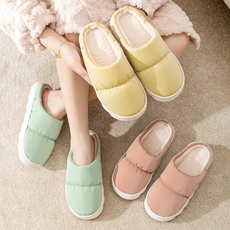 Blue down cotton indoor slippers with thick rubber sole and plush lining on a wooden floor.