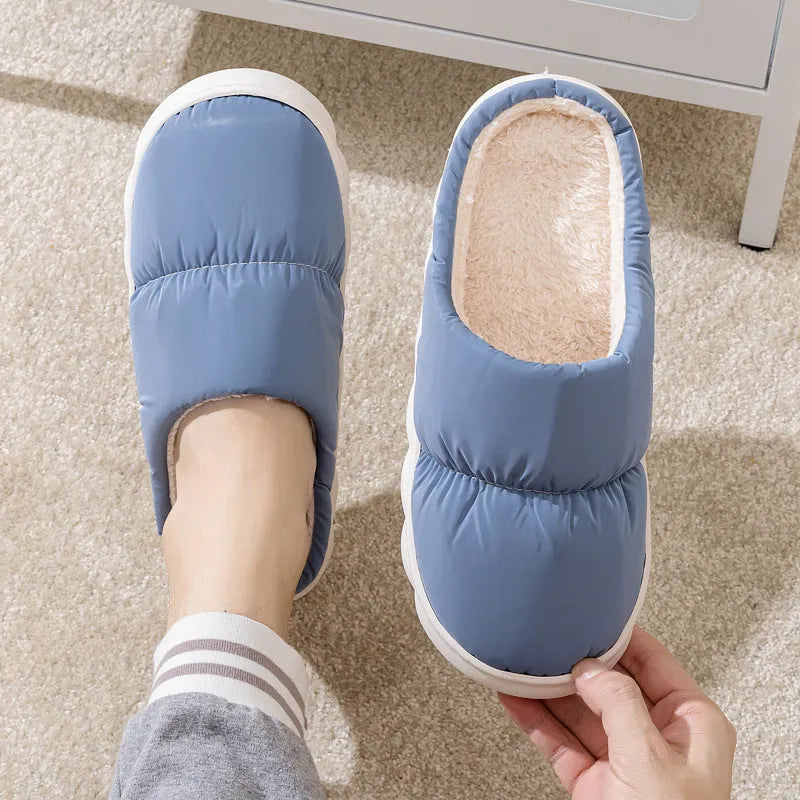 Blue down cotton indoor slippers with thick rubber sole and plush lining on a wooden floor.