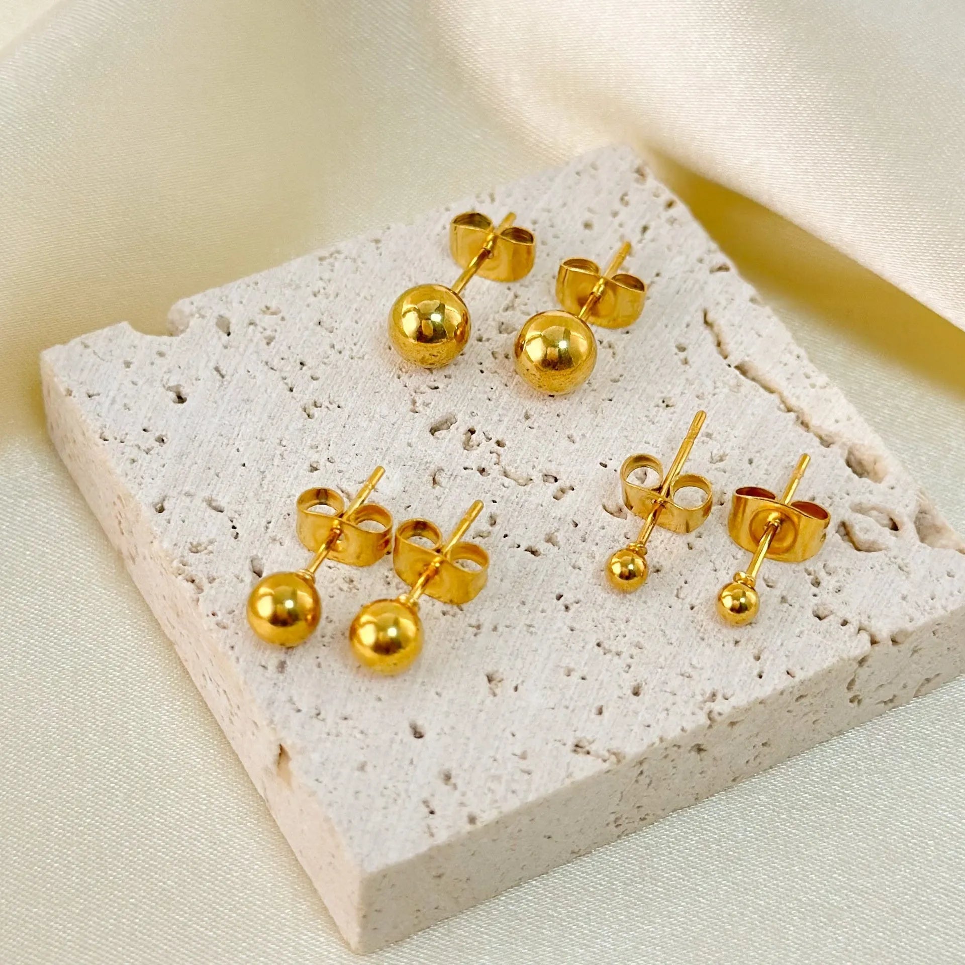 Stainless steel ball stud earrings in gold and silver finishes on a grey background.