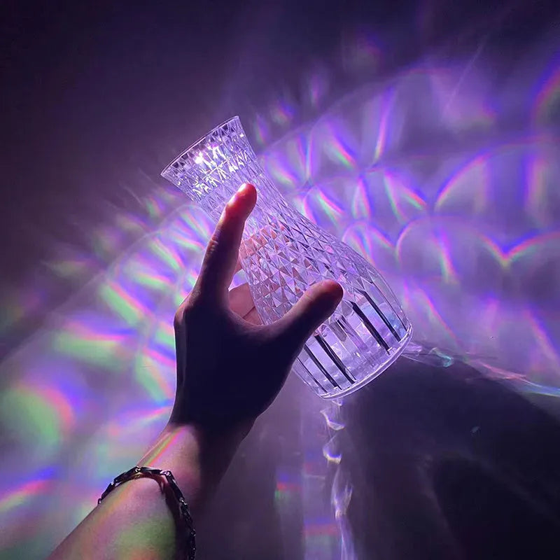 Clear plastic vase-shaped crystal bedside lamp with LED lights on a wooden table.
