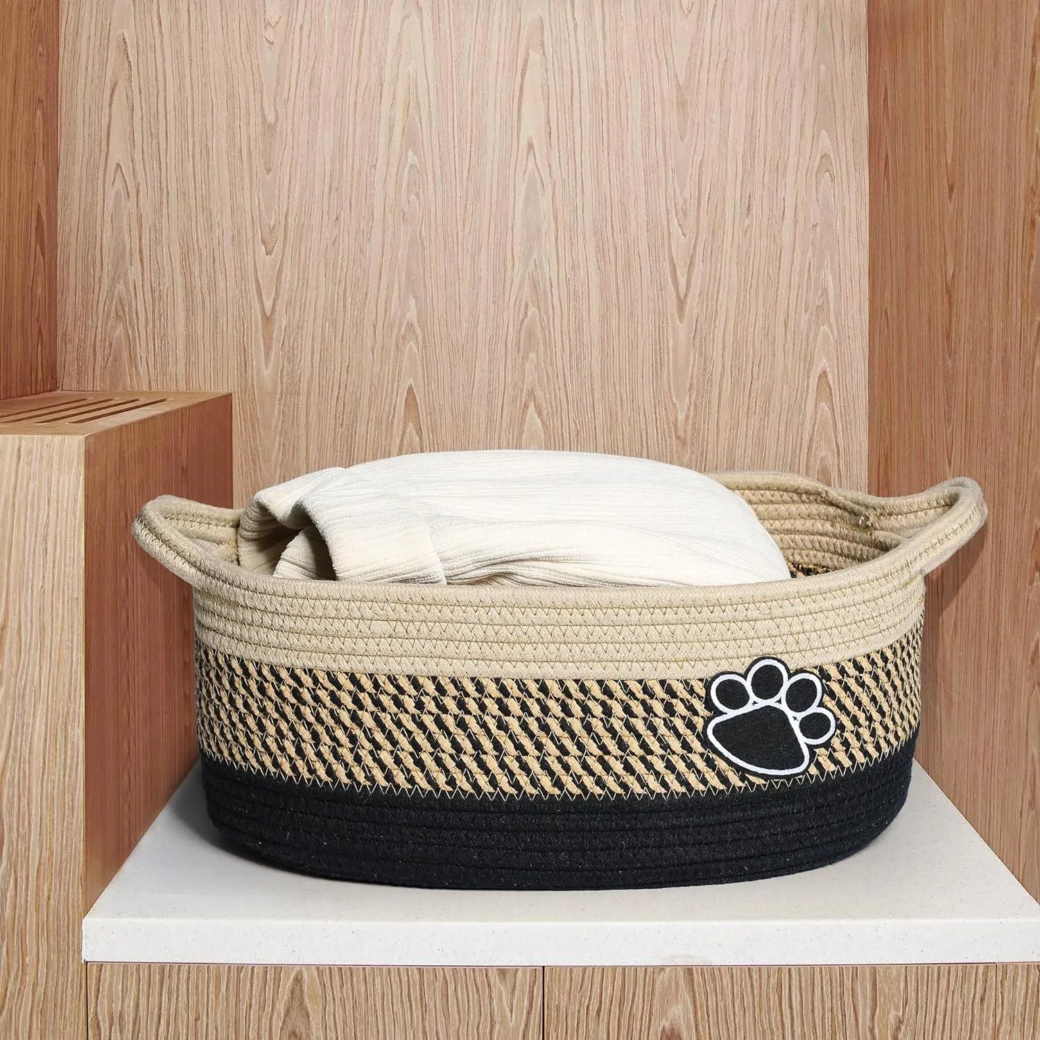 Light beige handmade woven cotton rope storage basket with handle on a wooden surface.