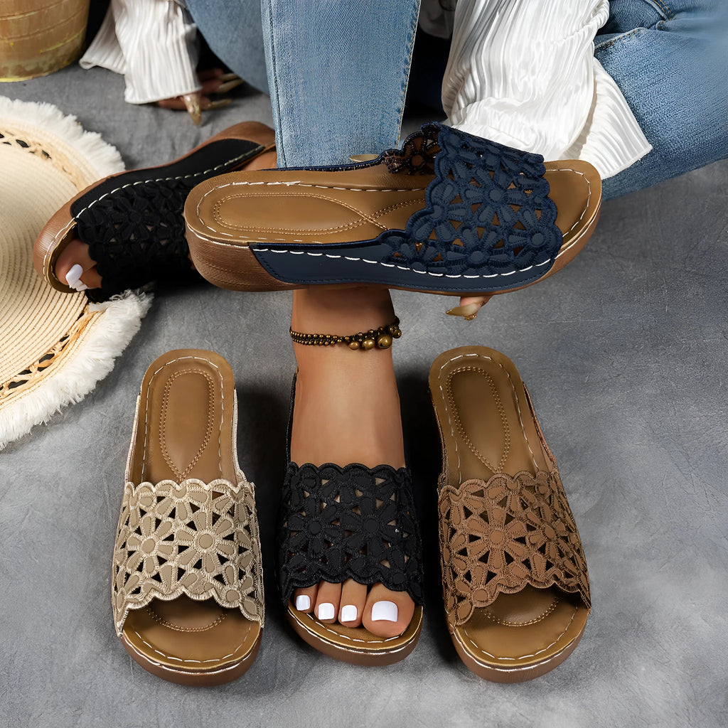Women's black beach slippers with flower cutout design on the PVC upper and a rubber wedge sole.