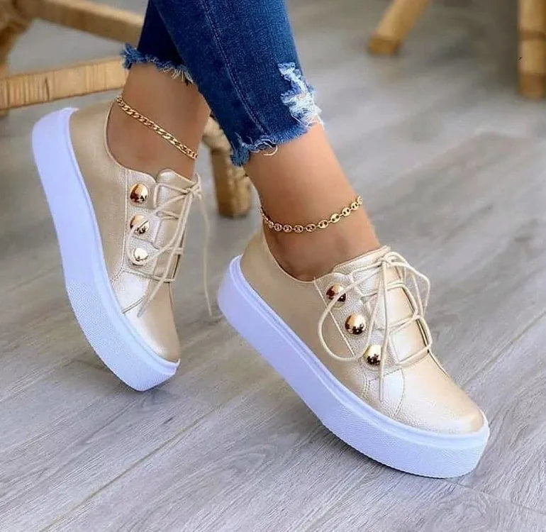 Women's white lace-up flats sneakers with silver rivet details on the low upper and a round toe.