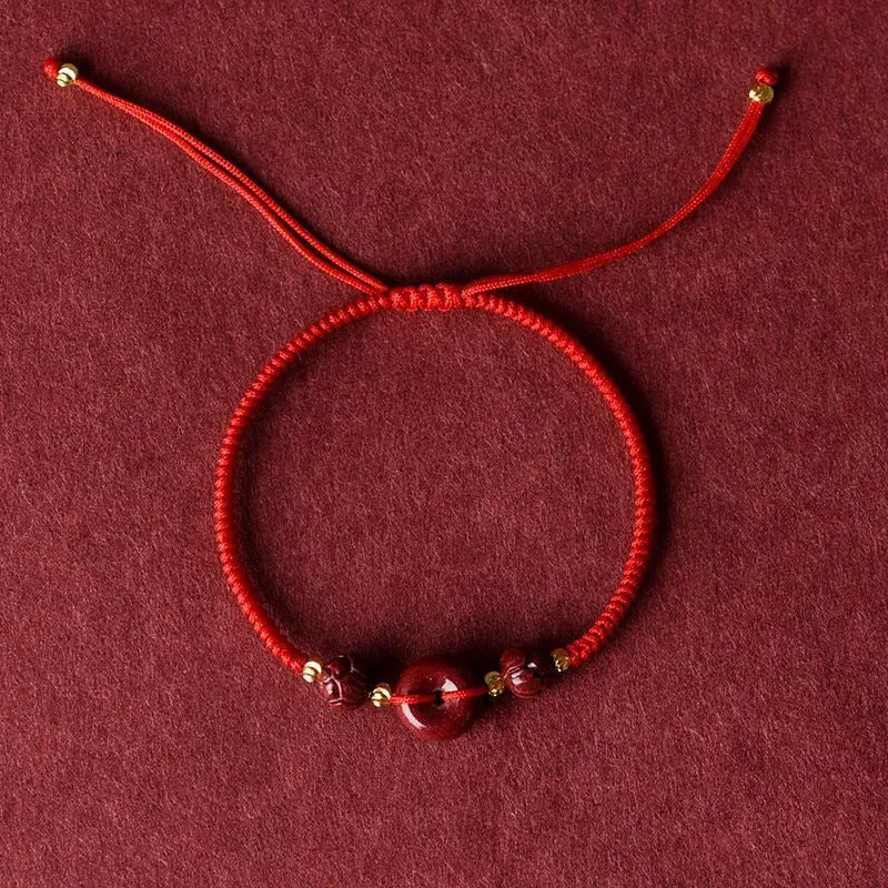 Heart-shaped cinnabar bead on an adjustable knot rope bracelet with a decorative peace buckle closure.