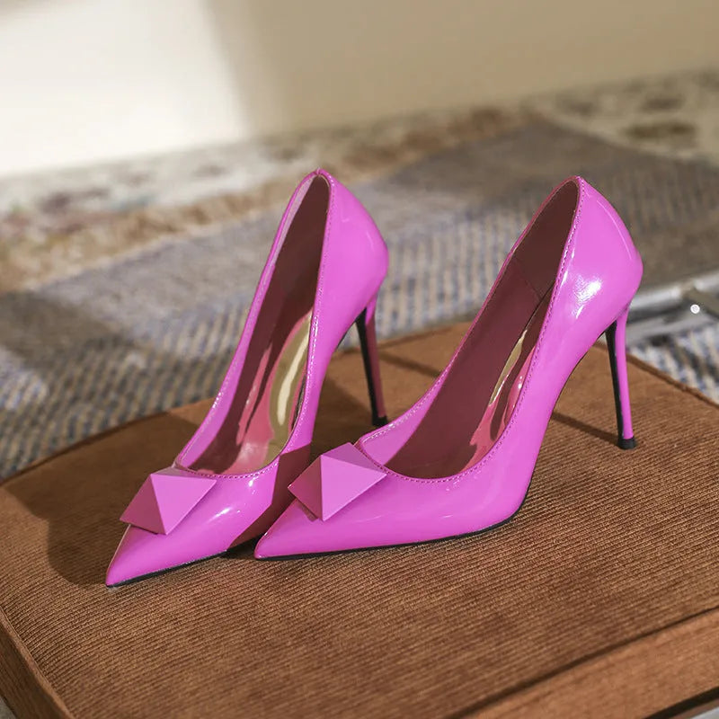 Pink women's pointed toe stiletto high heels with patent leather upper, rivet details, and a buckle.
