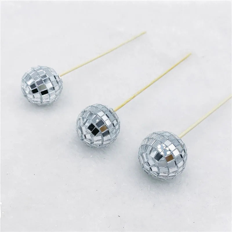 Glass disco ball cake decoration with wooden stick on a cake, showing reflective surface.