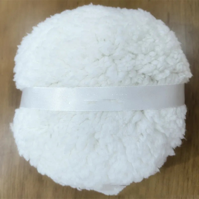 Large oval white plush powder puff for makeup on a plain background.