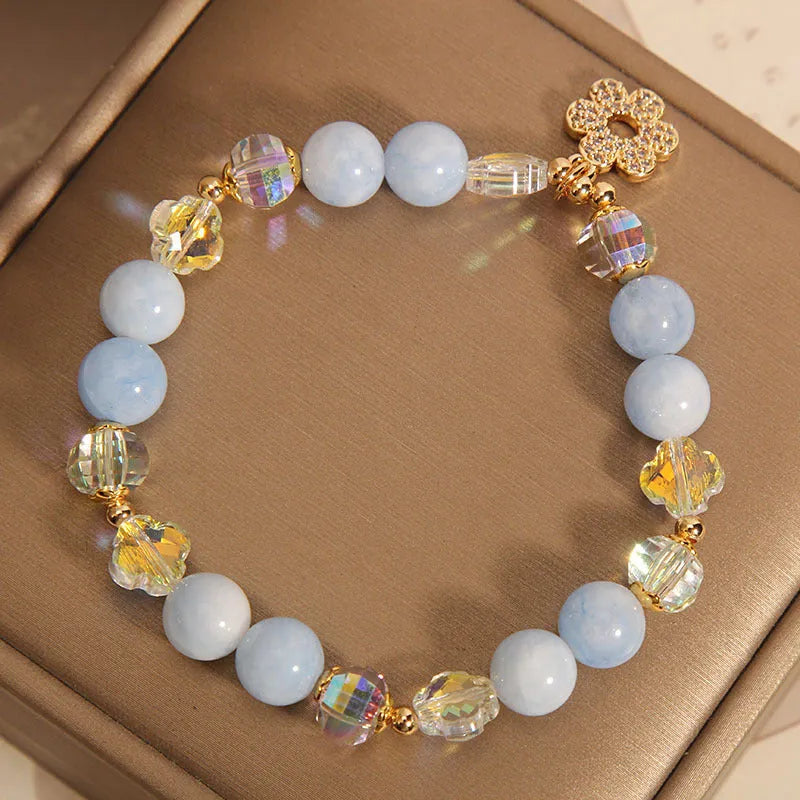 Women's aquamarine crystal bracelet with a four-leaf clover charm and a pearl accent on a model's wrist.