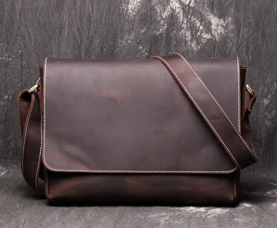 Vintage brown cowhide leather messenger bag with a shoulder strap, shown open to reveal internal ID, phone, and zipper pockets.