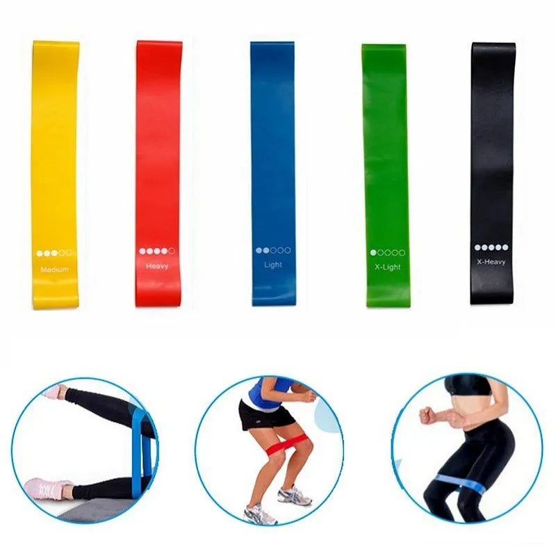 Set of five colour-coded yoga resistance straps in green, blue, yellow, red, and black on a gym mat.