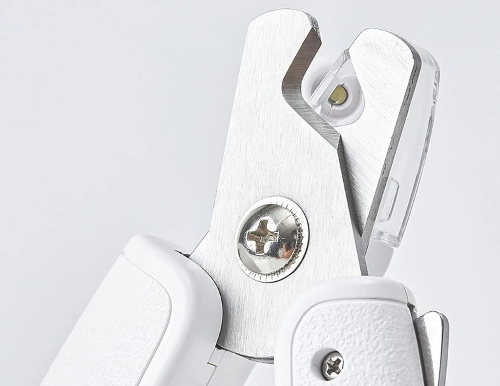 White pet nail clippers with LED light, anti-splash guard, and a nail file on a table.
