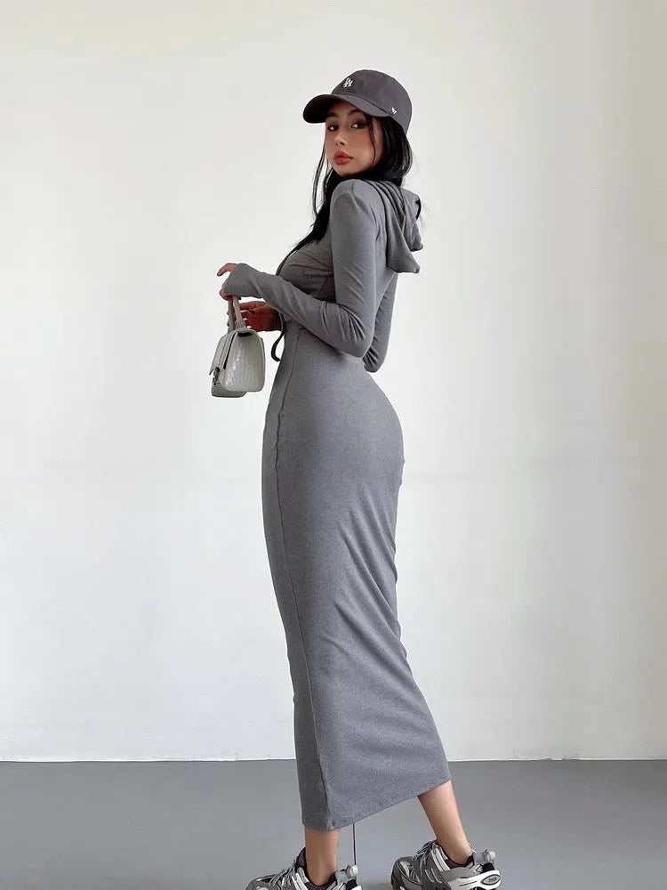 A woman wearing a grey high-waist hooded long sleeve sheath dress, knee-length pullover style.