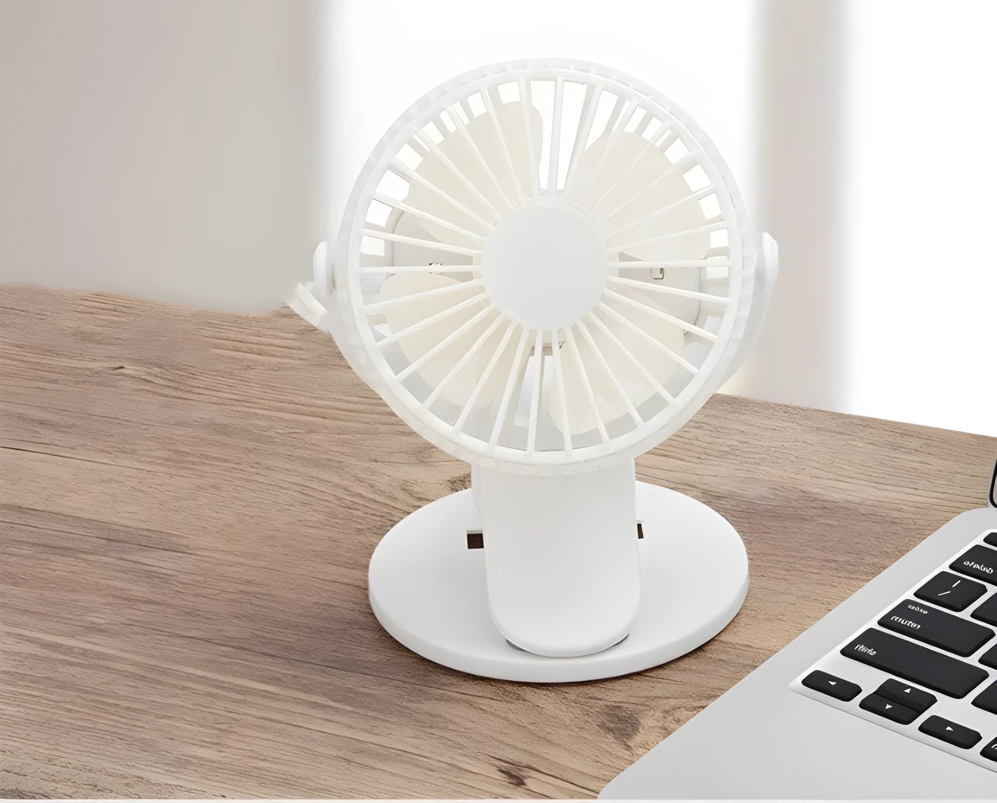 Small white clip fan with USB cable attached to a desk edge