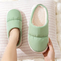 Blue down cotton indoor slippers with thick rubber sole and plush lining on a wooden floor.