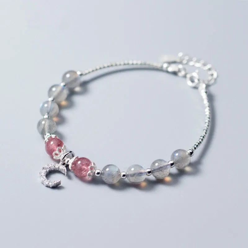 Natural moonstone bracelet with round beads, a crescent moon charm, and an adjustable silver chain on a wrist.