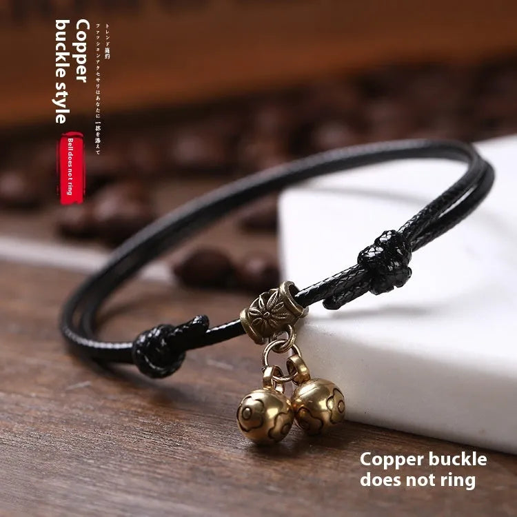 Black nylon rope dog collar with an attached brass bell lying on a wooden surface.