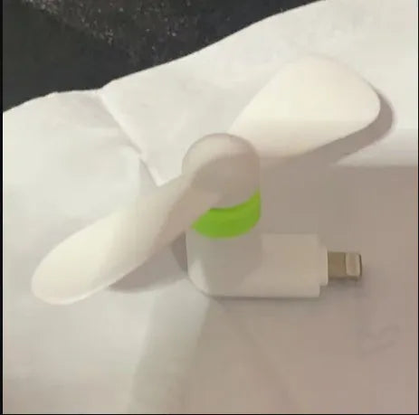White portable mini fan with plastic blades and rotary switch attached to a mobile phone.