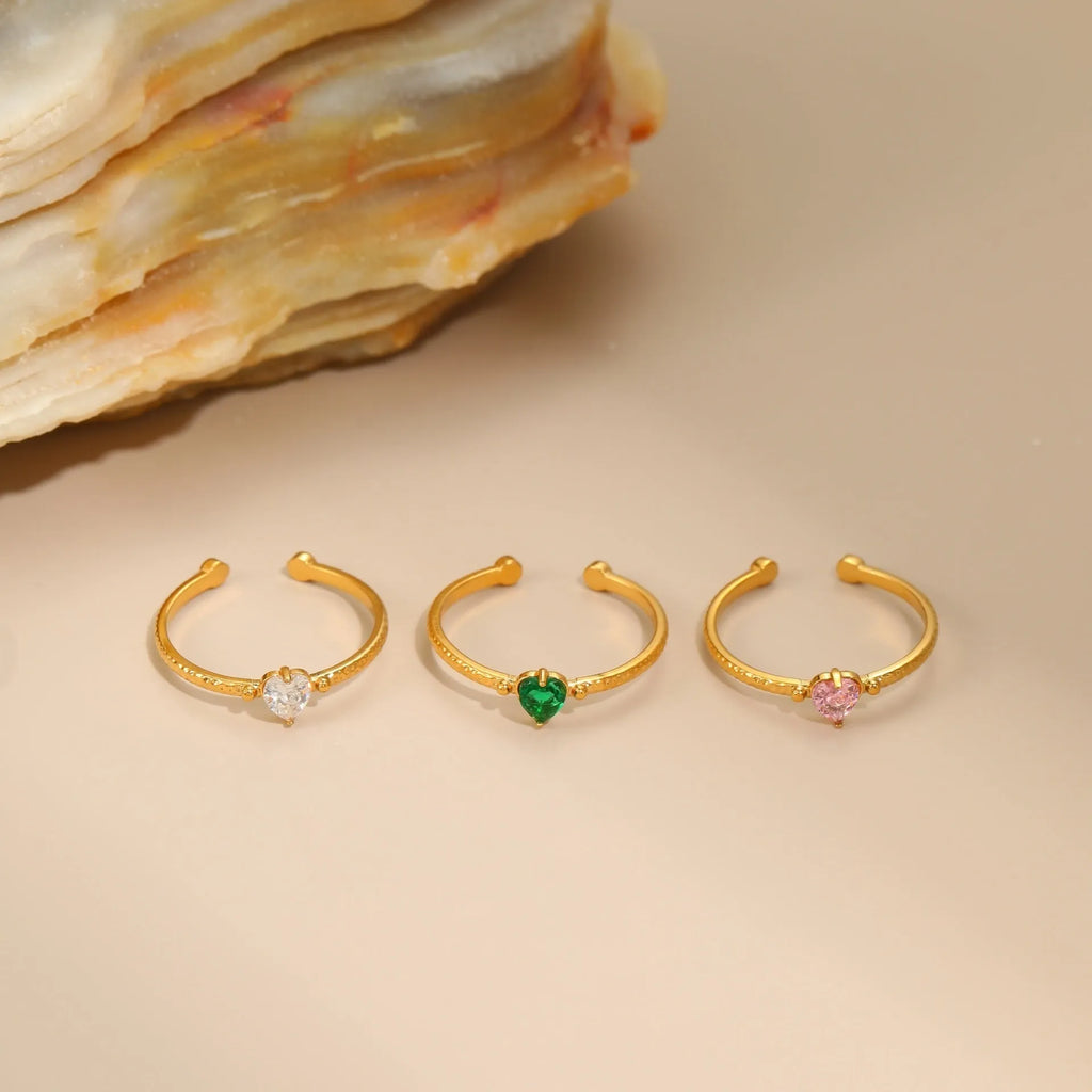 Open ended stainless steel ring with a geometric zircon-inlaid heart in white, pink, or green.