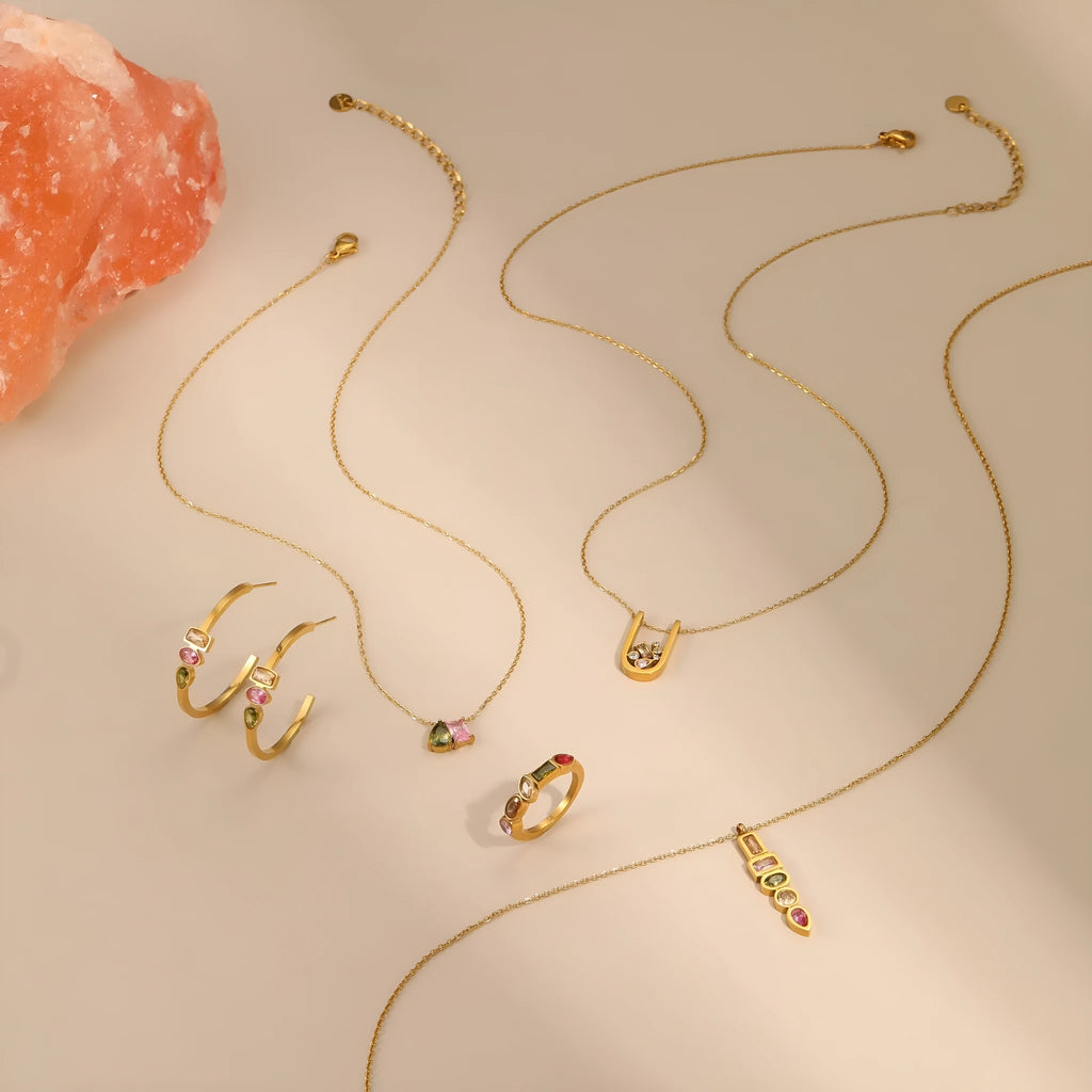 Geometric gold plated zircon jewellery set showing necklace, ring, and earrings on a grey background.