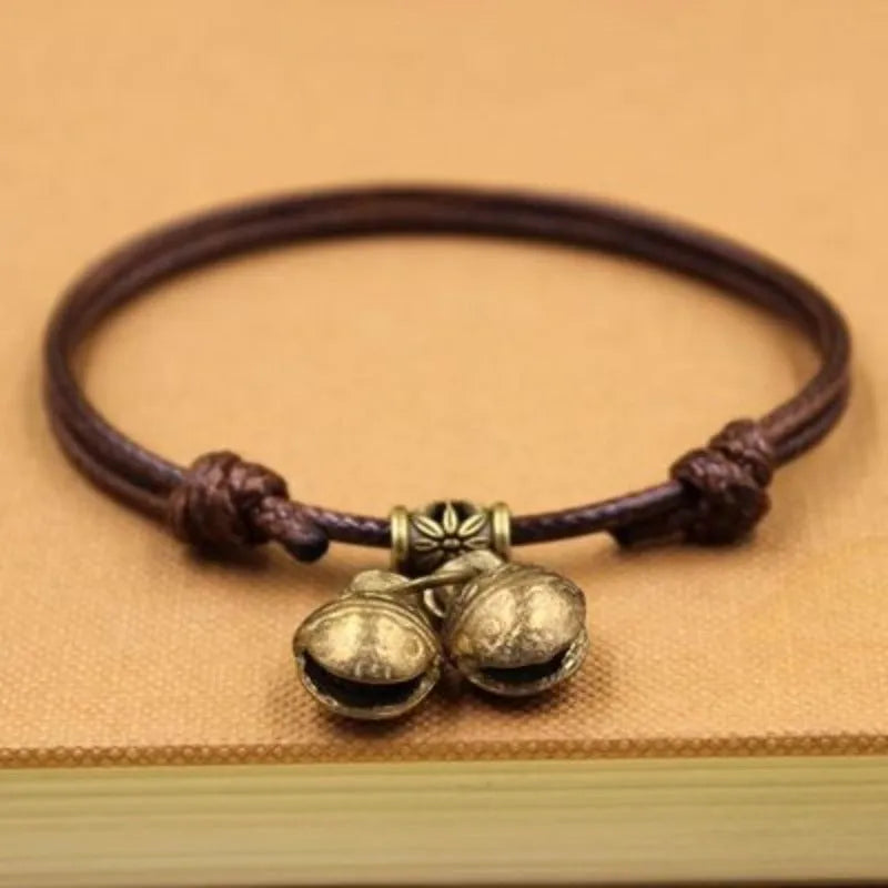Black nylon rope dog collar with an attached brass bell lying on a wooden surface.