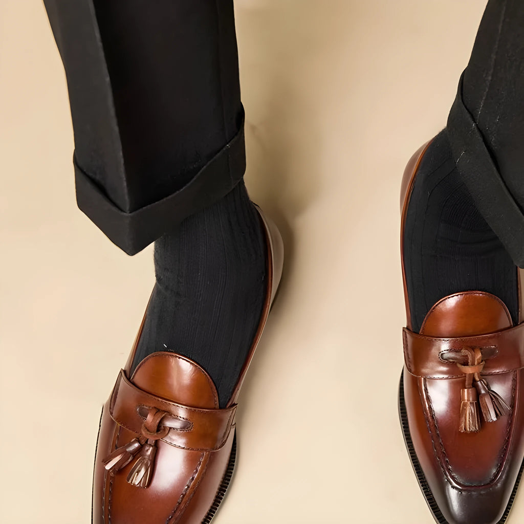Men's black polished leather tassel loafers on a white background