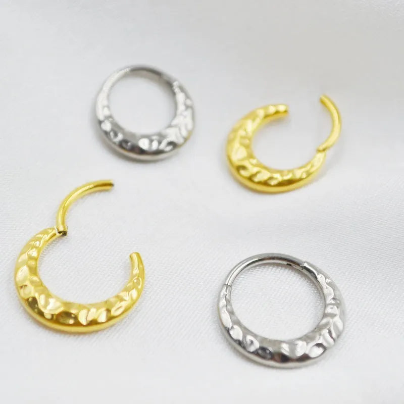 Close-up of a concave-convex carved titanium nose ring in gold finish on a grey background.
