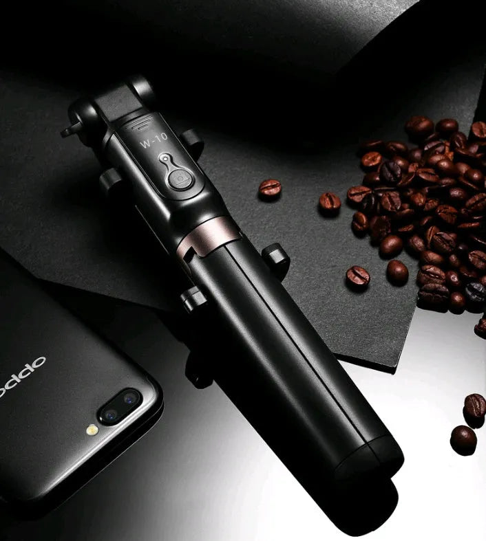 Black Bluetooth selfie stick tripod with extended rod, phone clamp, and deployed legs next to a smartphone