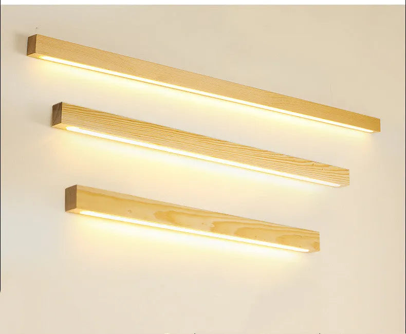 Slim walnut-coloured wooden strip LED wall lamp in three length options on a white wall.