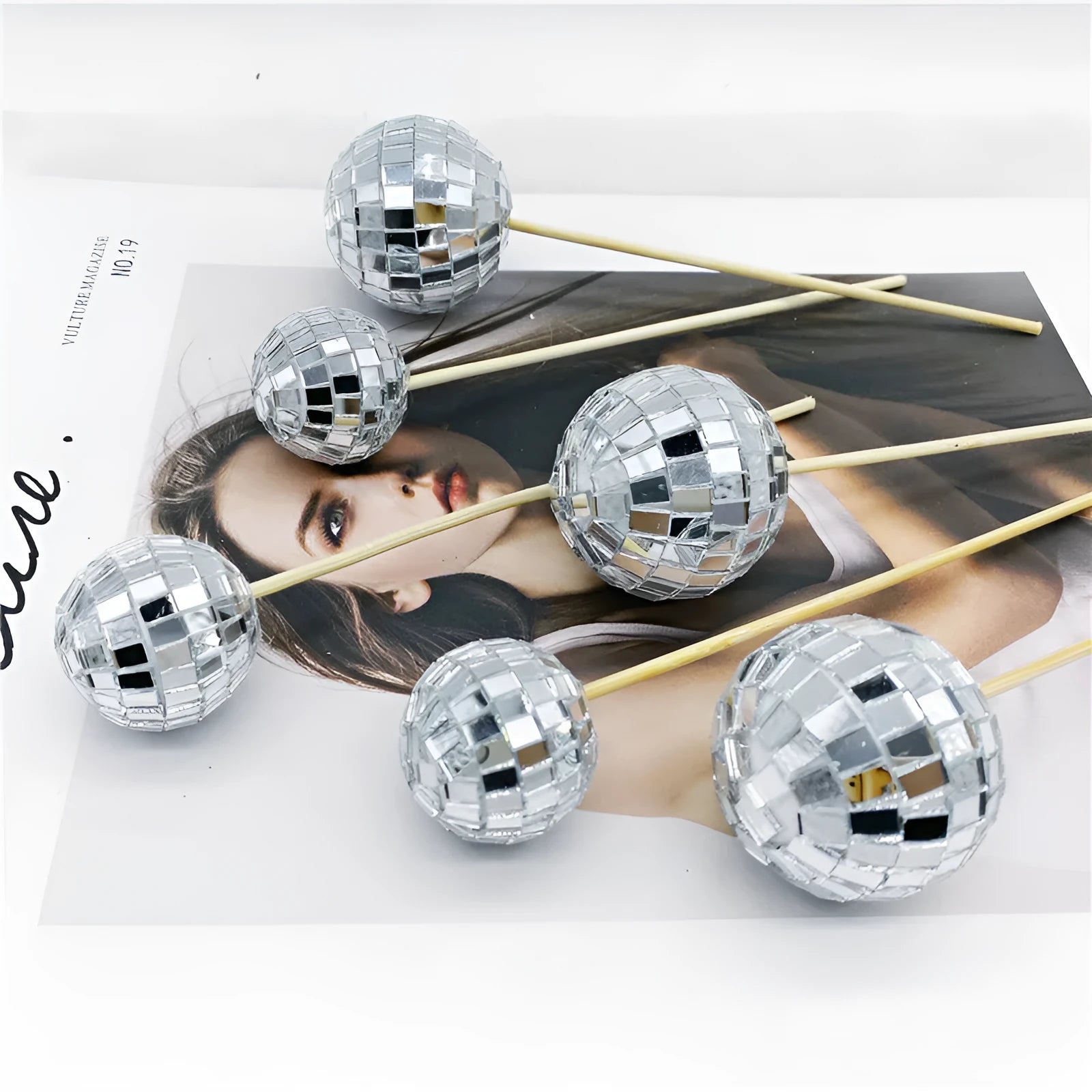 Glass disco ball cake decoration with wooden stick on a cake, showing reflective surface.