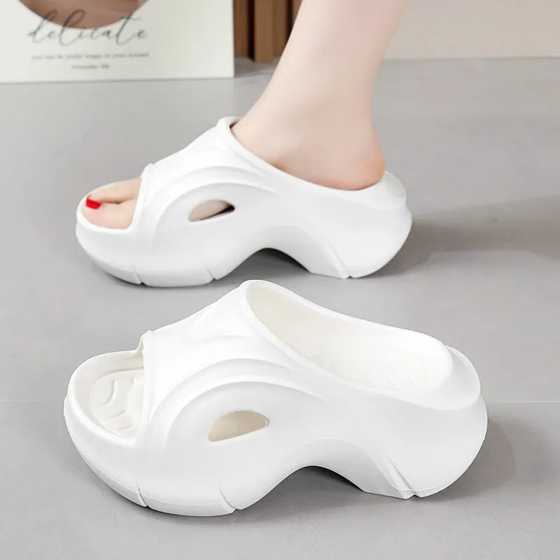 Women's white thick-soled EVA slippers with rounded toe on a sandy beach.
