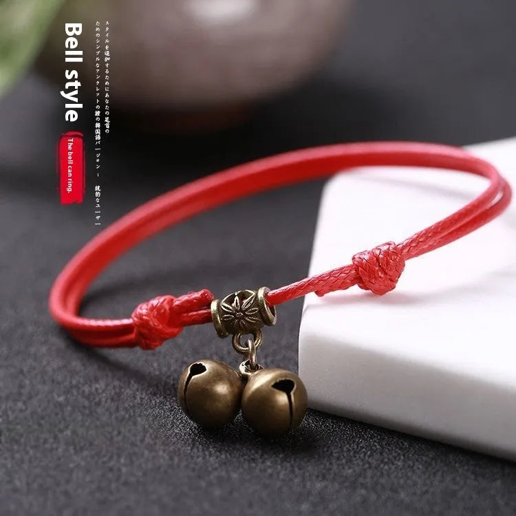 Black nylon rope dog collar with an attached brass bell lying on a wooden surface.