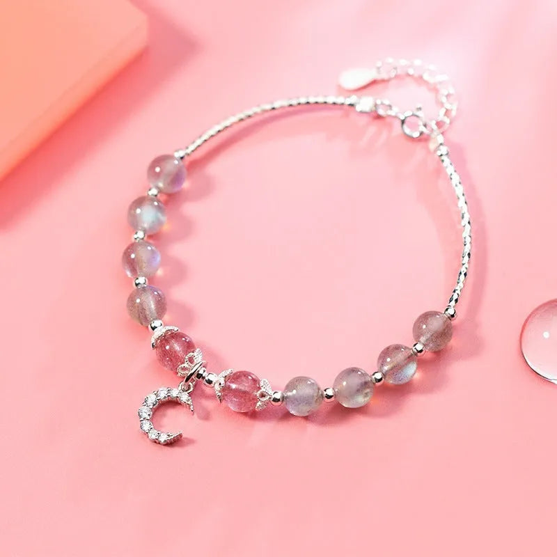 Natural moonstone bracelet with round beads, a crescent moon charm, and an adjustable silver chain on a wrist.