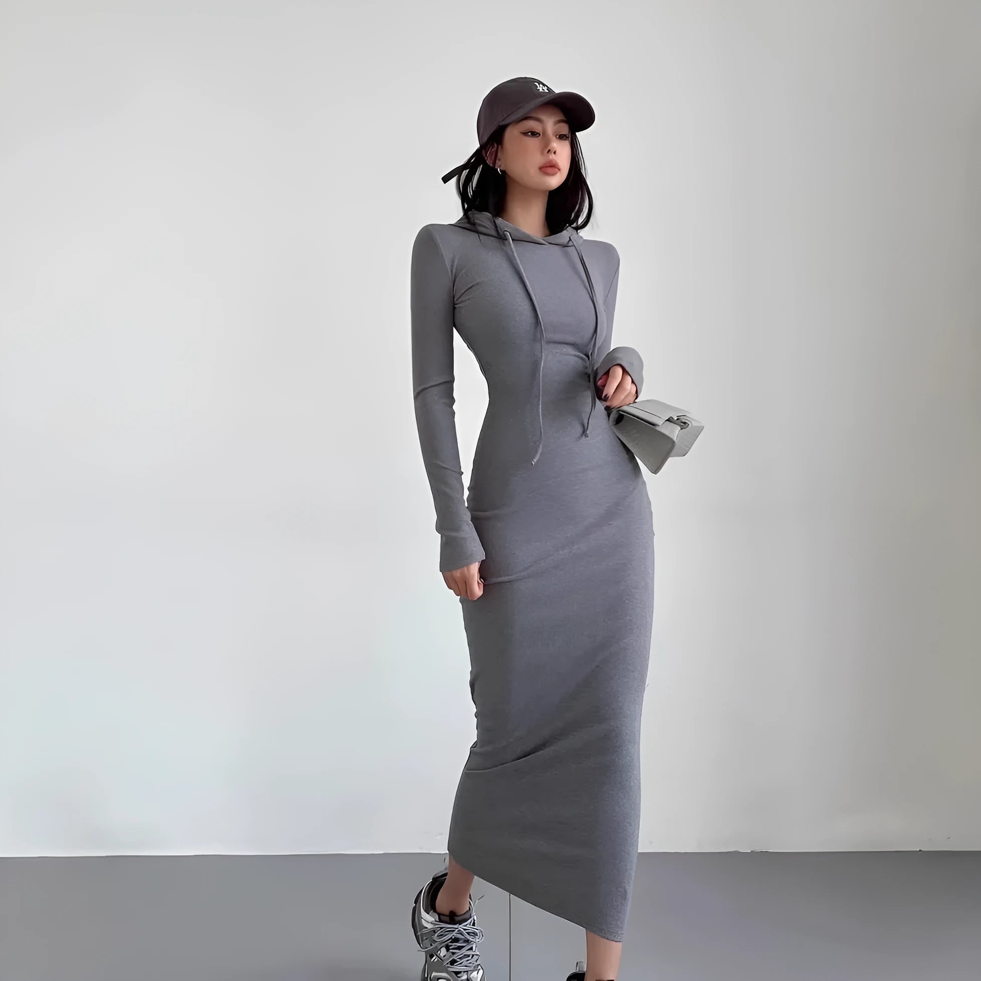 A woman wearing a grey high-waist hooded long sleeve sheath dress, knee-length pullover style.